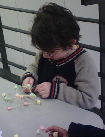 A young student building polyhedra with marshmallows and toothpicks